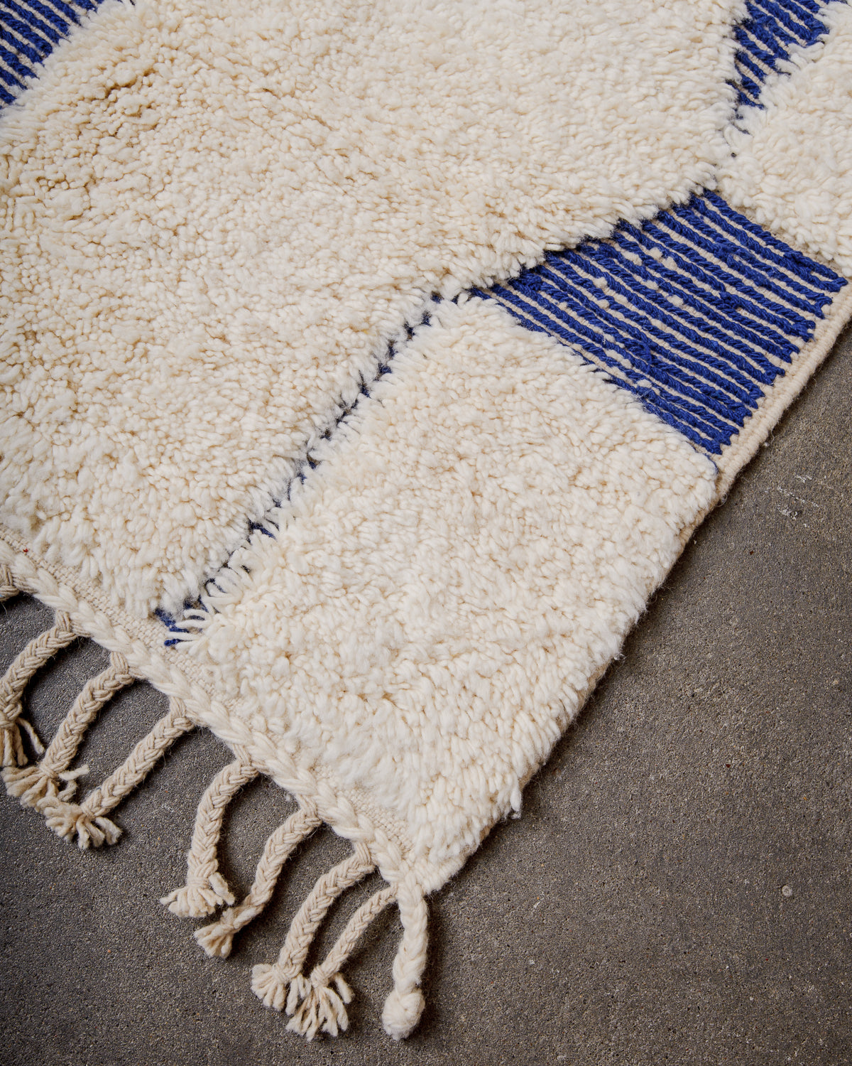 Corner of wool rug with tightly woven end and natural wool tassels.